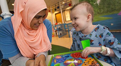 nurse plays a board game with a pediatric cancer patient